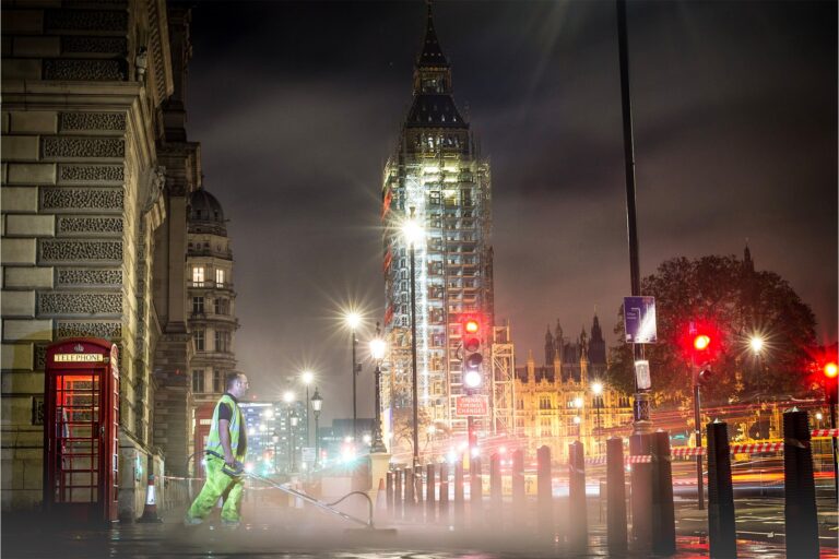 A cleaning crew pressure washing the pavement outside Big Ben in London, restoring the iconic landmark's surroundings to pristine condition.