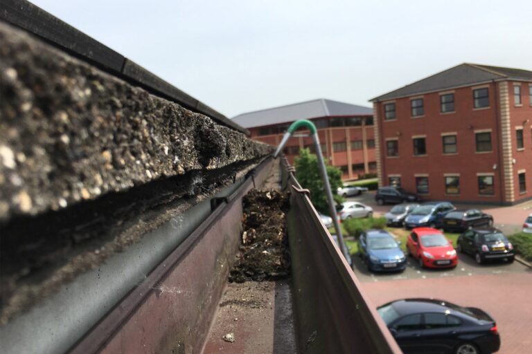 A professional gutter cleaner using a SkyVac gutter vacuum to empty gutters on a block of flats in Leighton Buzzard, demonstrating high-efficiency cleaning.